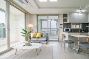 A modern apartment with a dining area, kitchen, and a large window with a city view.