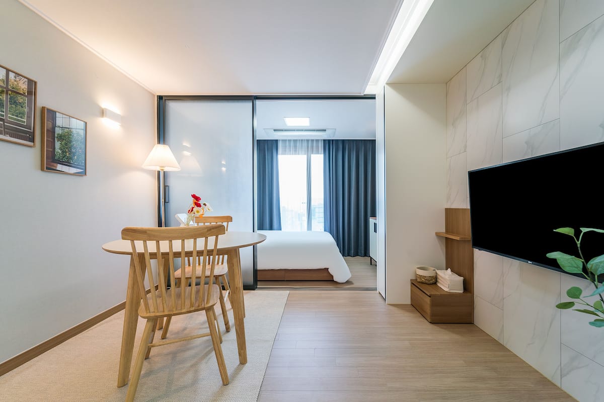 Une chambre d’hôtel avec un lit, une télévision, un bureau avec une chaise et une fenêtre avec des rideaux.