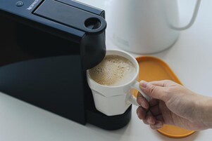 A hand holding a white coffee cup under a Nespresso coffee machine.
