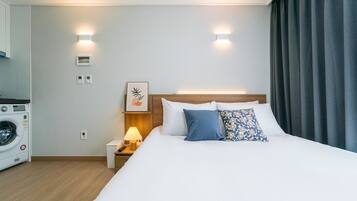 Hotelkamer met een bed, nachtkastje met lamp, wandbeugelthermostaat en een wasmachine in de hoek.