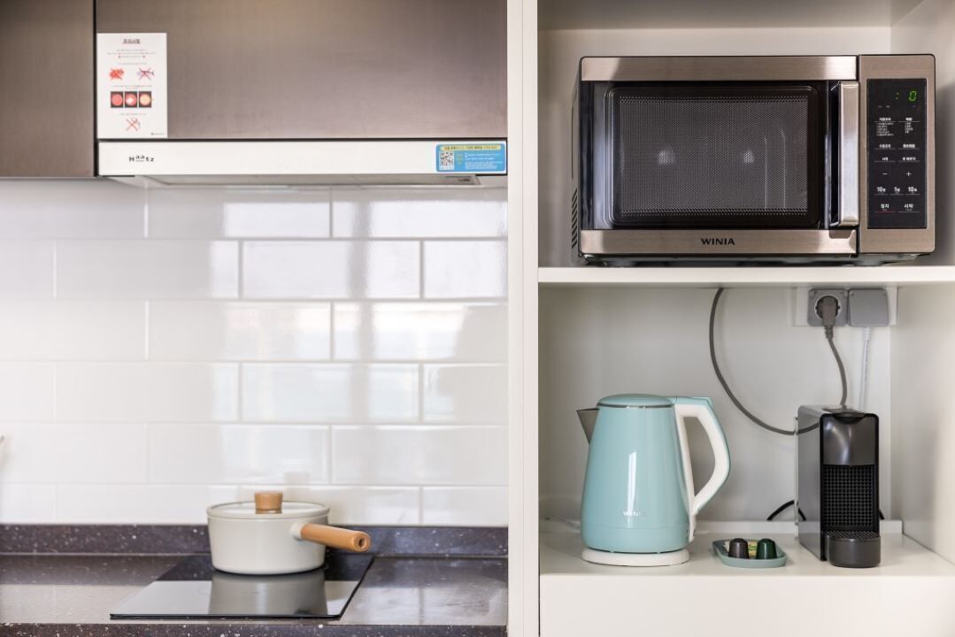 Una cucina con forno a microonde, bollitore e macchina del caffè sul bancone.
