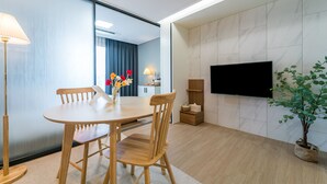 A modern hotel room with a dining area, a flat-screen TV mounted on the wall, and a potted plant. - Urbanstay Jeju Airport (Jeju City)