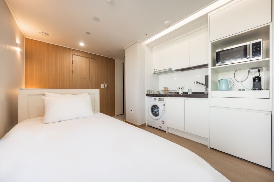 A modern hotel room with a large bed, a washing machine, a microwave, and a coffee maker.