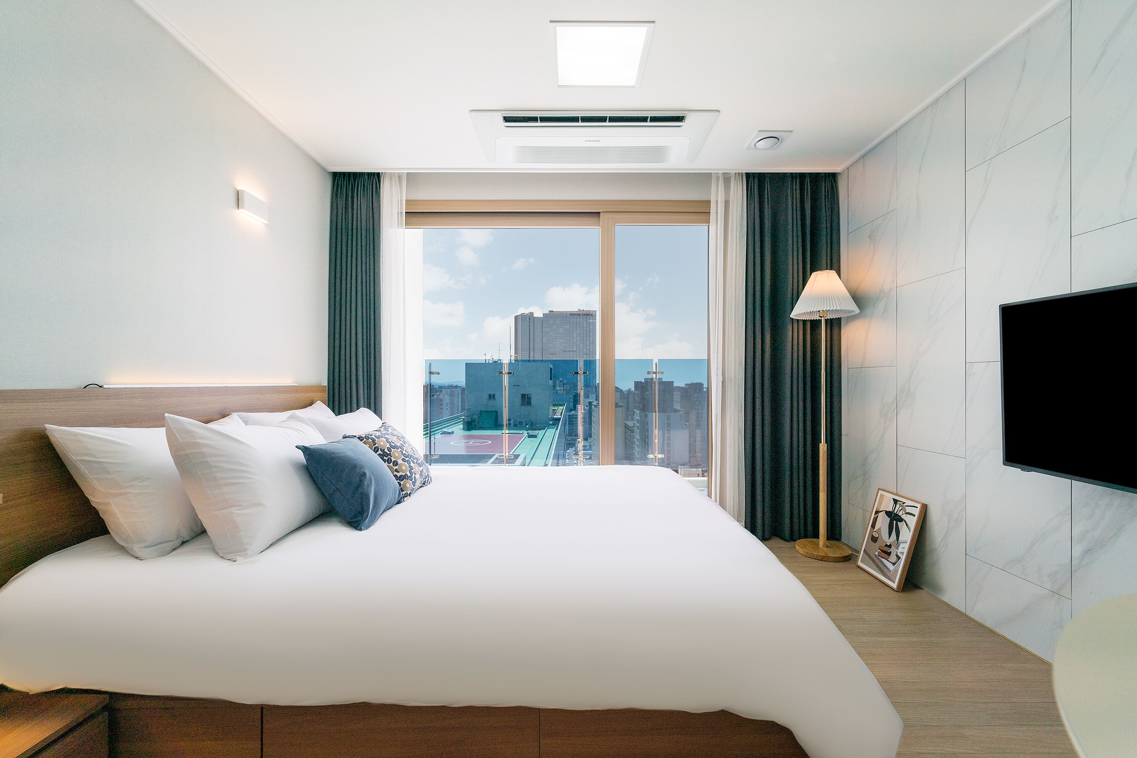 Une chambre d’hôtel moderne dotée d’un grand lit, d’un téléviseur à écran plat, d’une vue sur la ville et d’un luminaire au plafond.