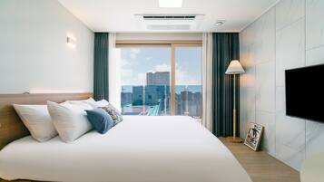 A modern hotel room with a large bed, a flat-screen TV, a city view, and a ceiling light.
