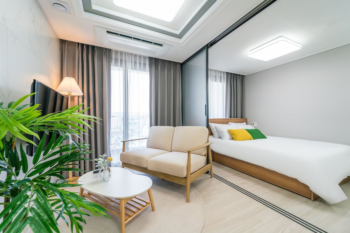 Une chambre d’hôtel moderne avec un canapé, une petite table ronde, un lit et une grande fenêtre avec des rideaux.