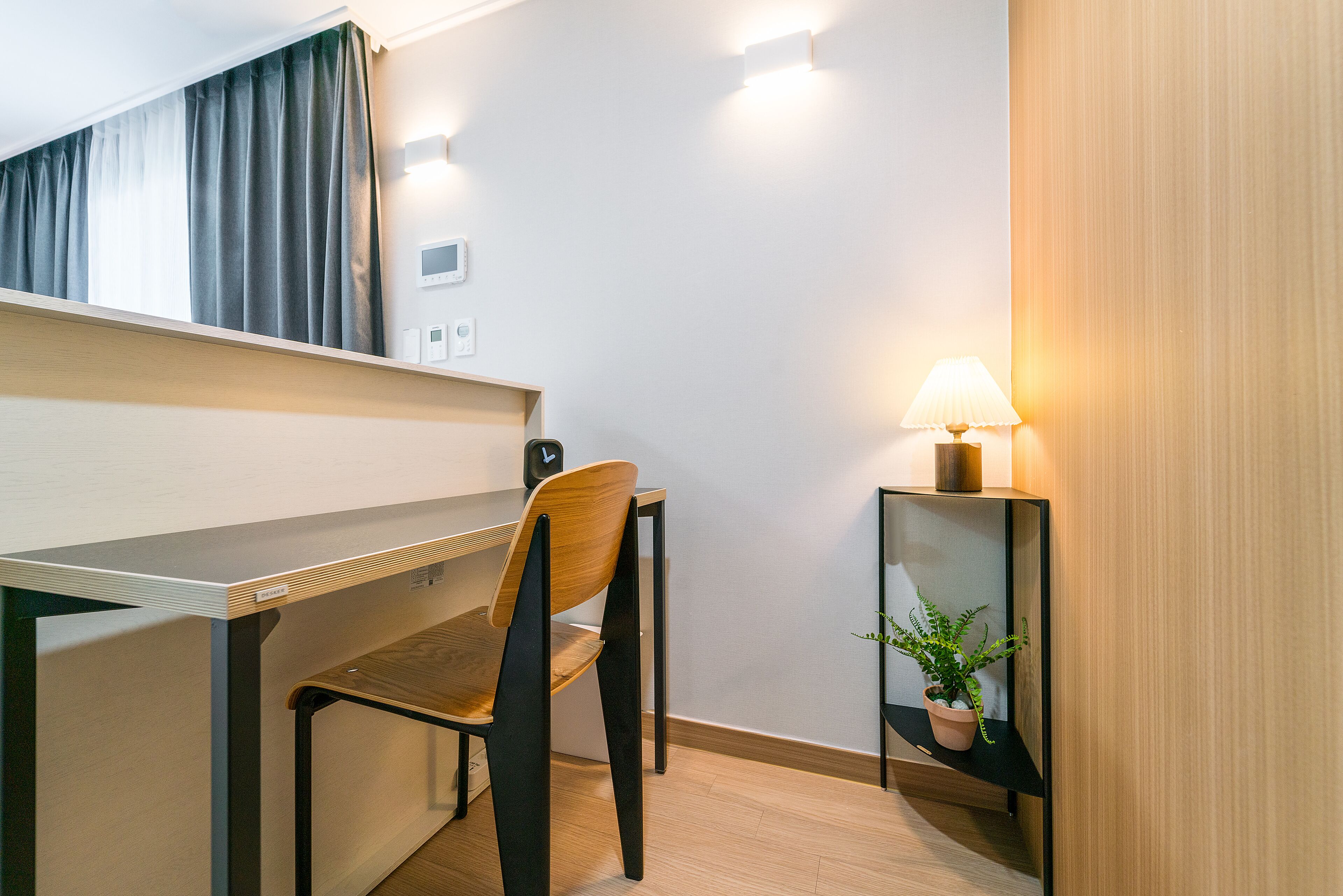Een moderne kamer met een bureau, stoel, lamp en een potplant.