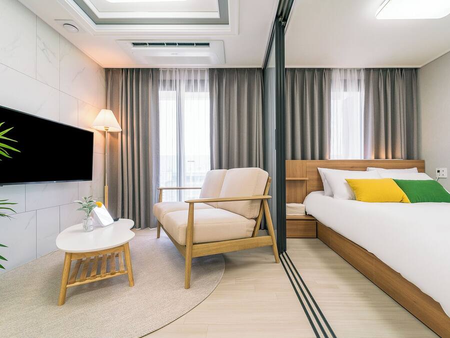 A modern hotel room with a bed, a chair, a small table, and a TV.