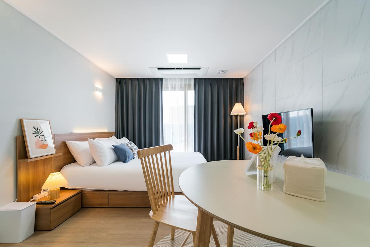 Une chambre d’hôtel moderne équipée d’un lit, d’une table de chevet, d’une lampe, d’une télévision et d’un coin repas avec une chaise et une table.