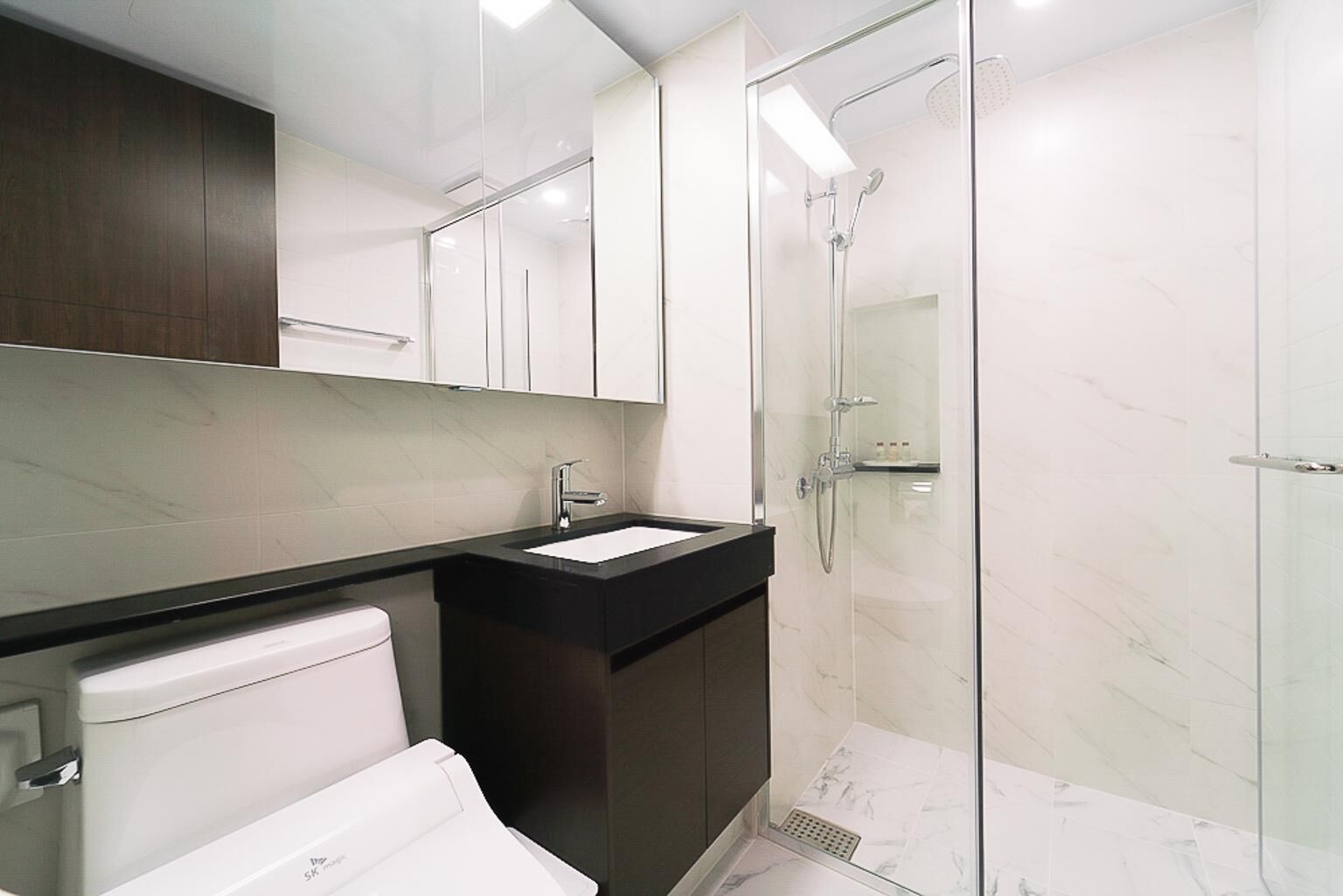 Un bany modern amb dutxa d'envidriament, un lavabo blanc i mobles de tons foscos.