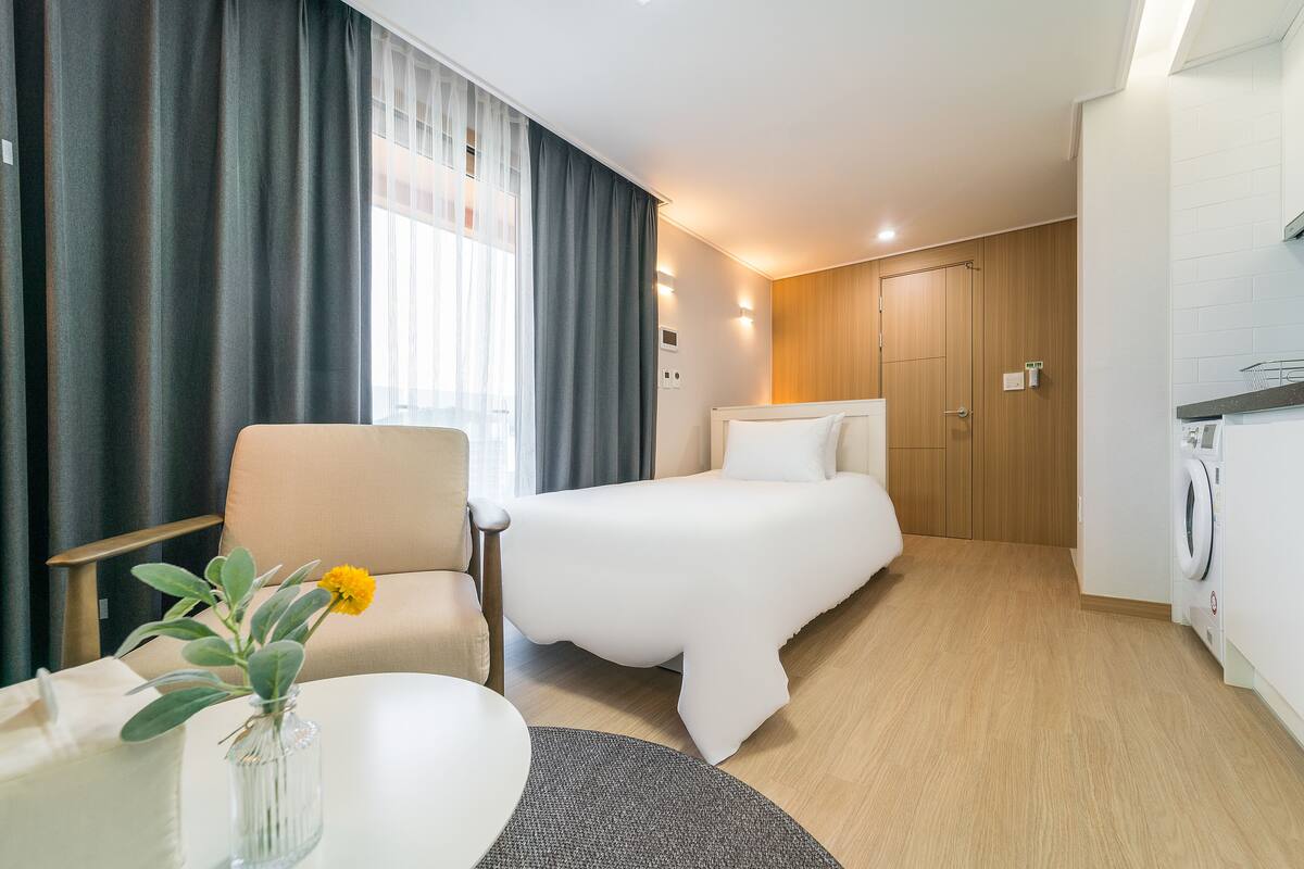 Une chambre d’hôtel avec un lit, une chaise, une table et un vase de fleurs.