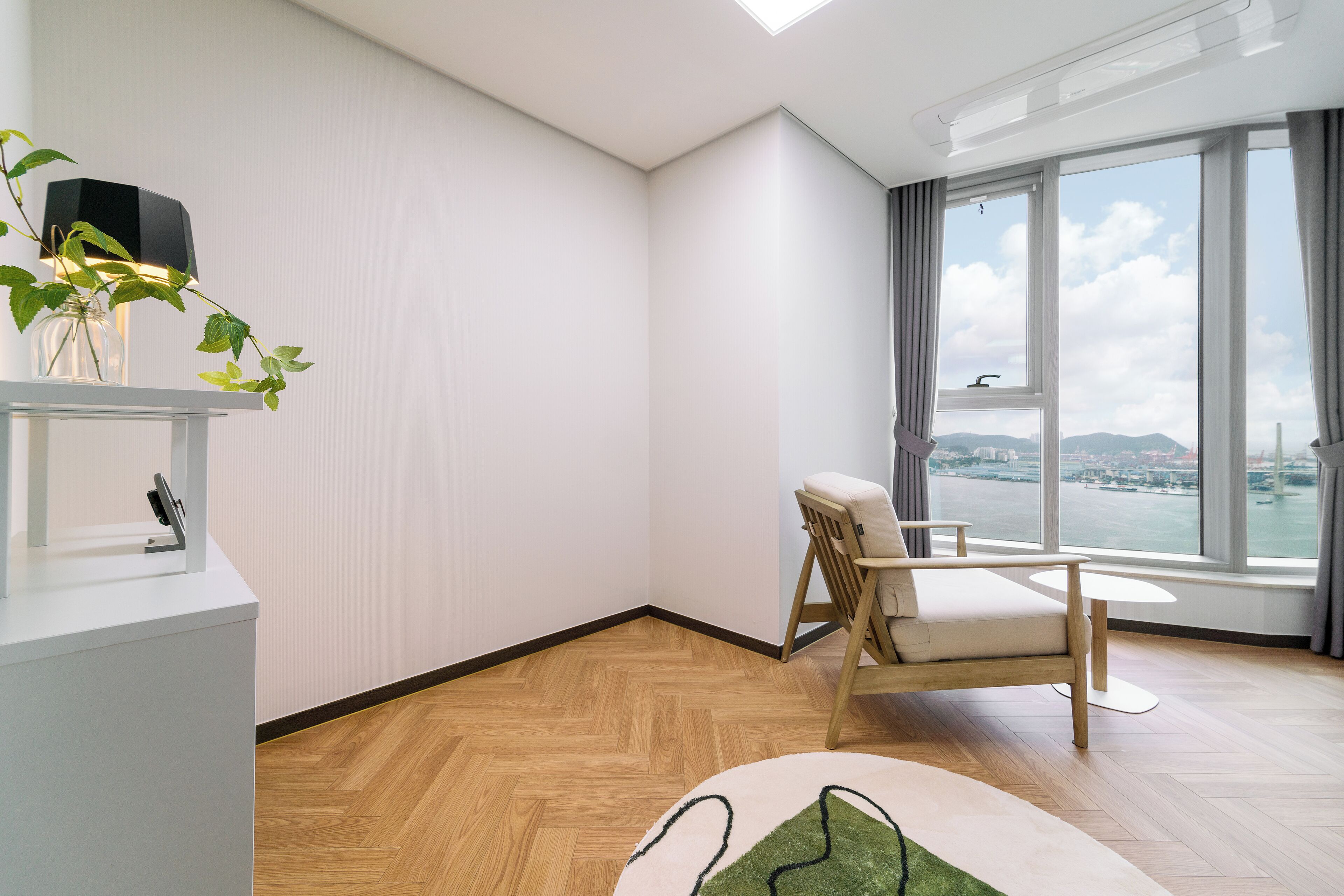 A modern room with a wooden floor, a sofa, a small table, and a large window offering a city view.