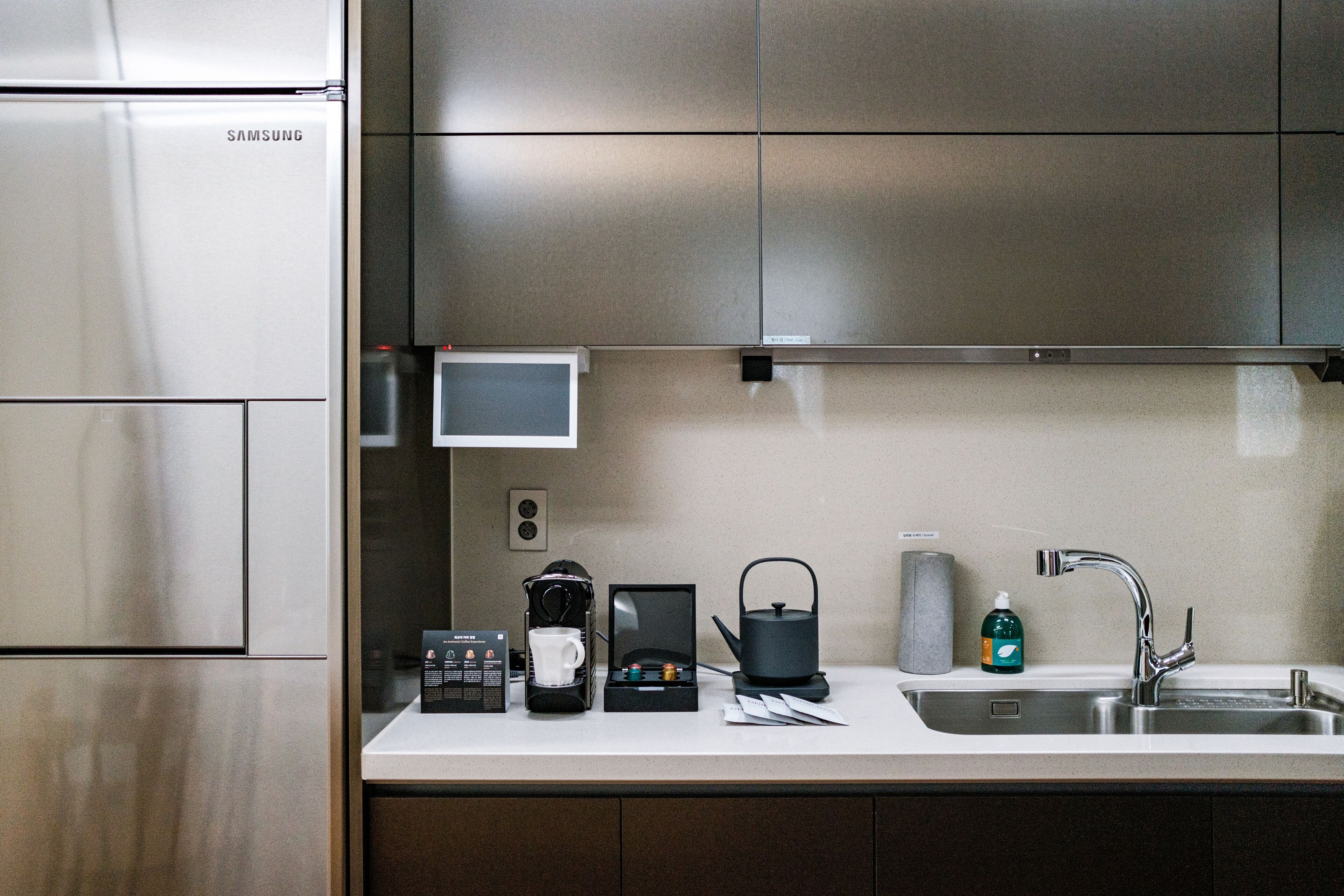A modern kitchen with stainless steel appliances, a coffee maker, a kettle, and a sink.