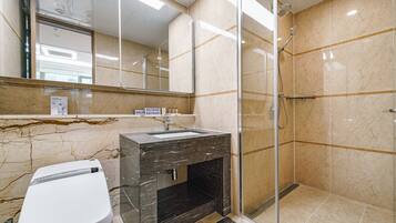A modern bathroom with a glass-enclosed shower, a marble vanity, and a large mirror.