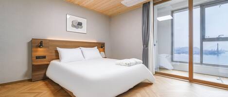 A modern hotel room with a wooden ceiling, a large bed, a view of a cityscape, and a sliding glass door.