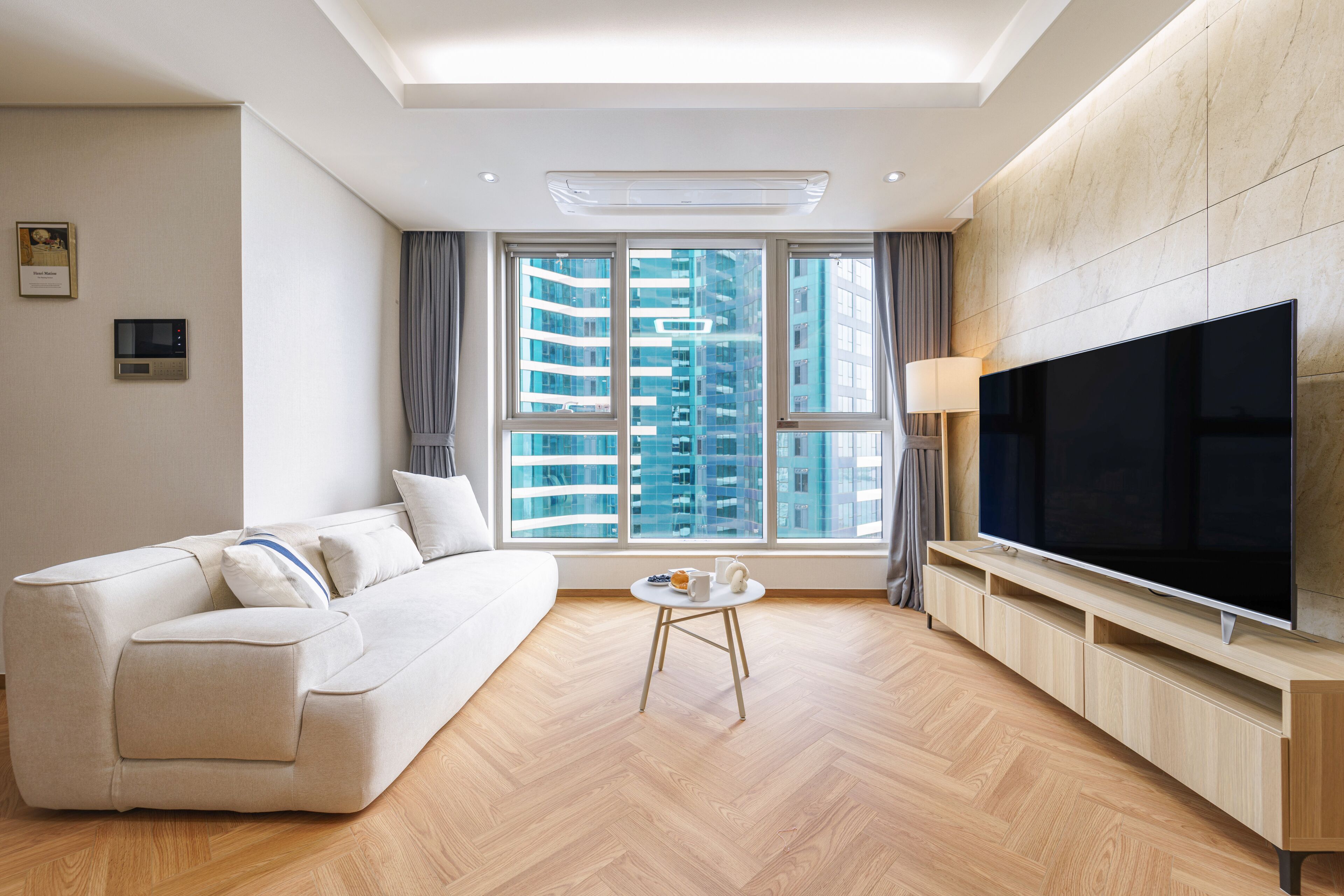 A modern living room with a sofa, a coffee table, a TV, and large windows with a city view.