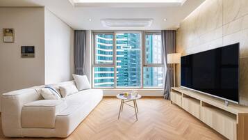 A modern living room with a sofa, a coffee table, a TV, and large windows with a city view.