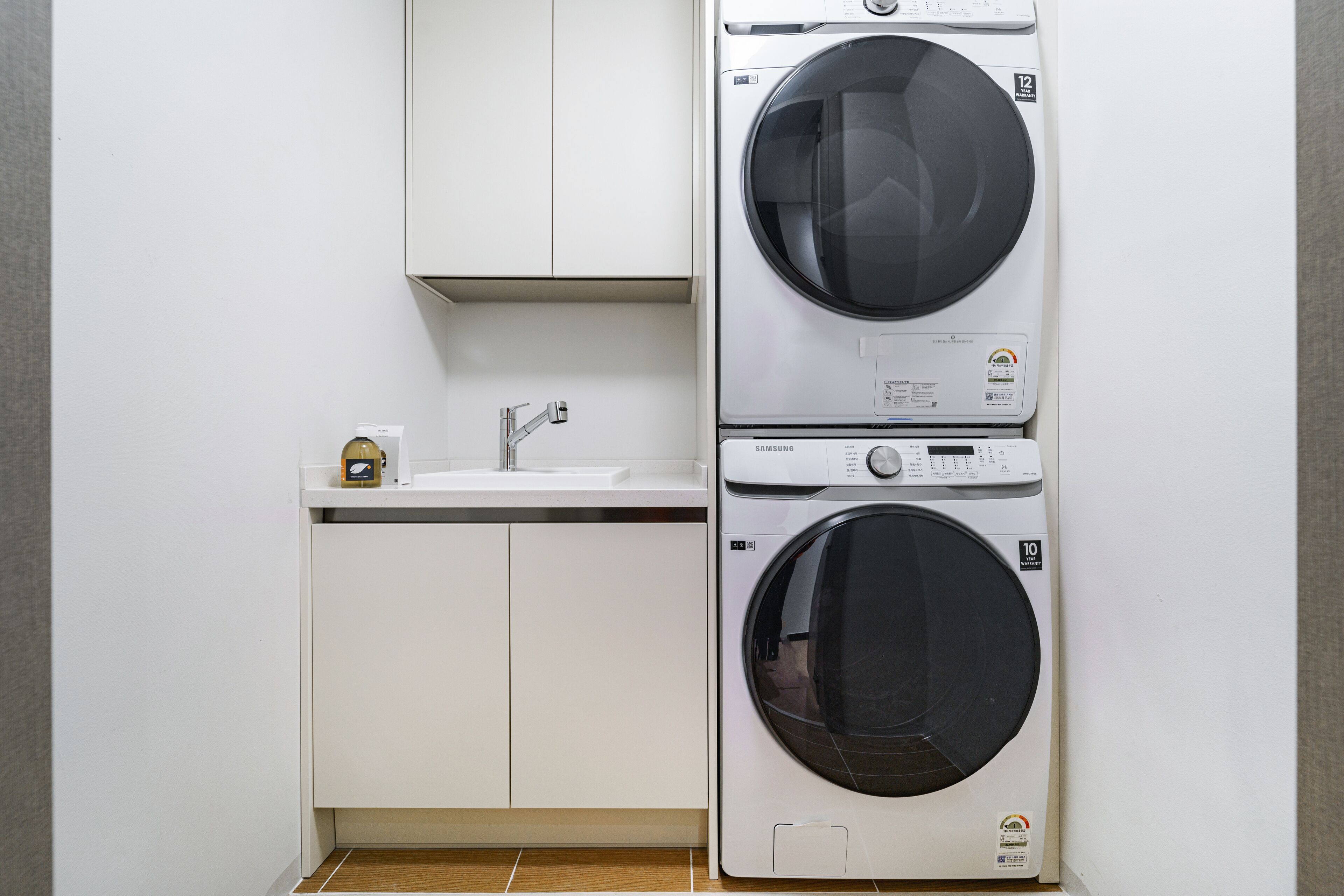 Un área de lavandería compacta con dos lavadoras apiladas, un lavabo y un armario.