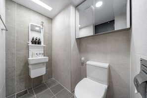 Un baño moderno con inodoro, lavamanos con espejo y zona de ducha.