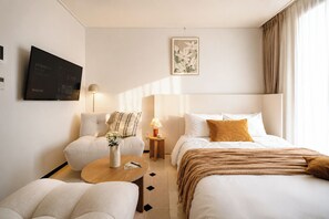 Habitación de hotel con cama, dos sillones, una mesa de centro, televisión y un cuadro en la pared.