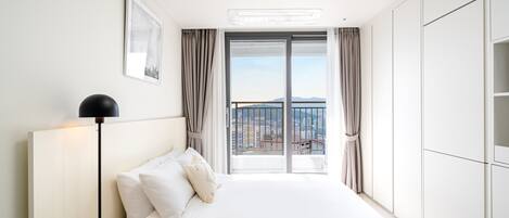 A hotel room with a large bed, a view of the city through a balcony, and a ceiling light.