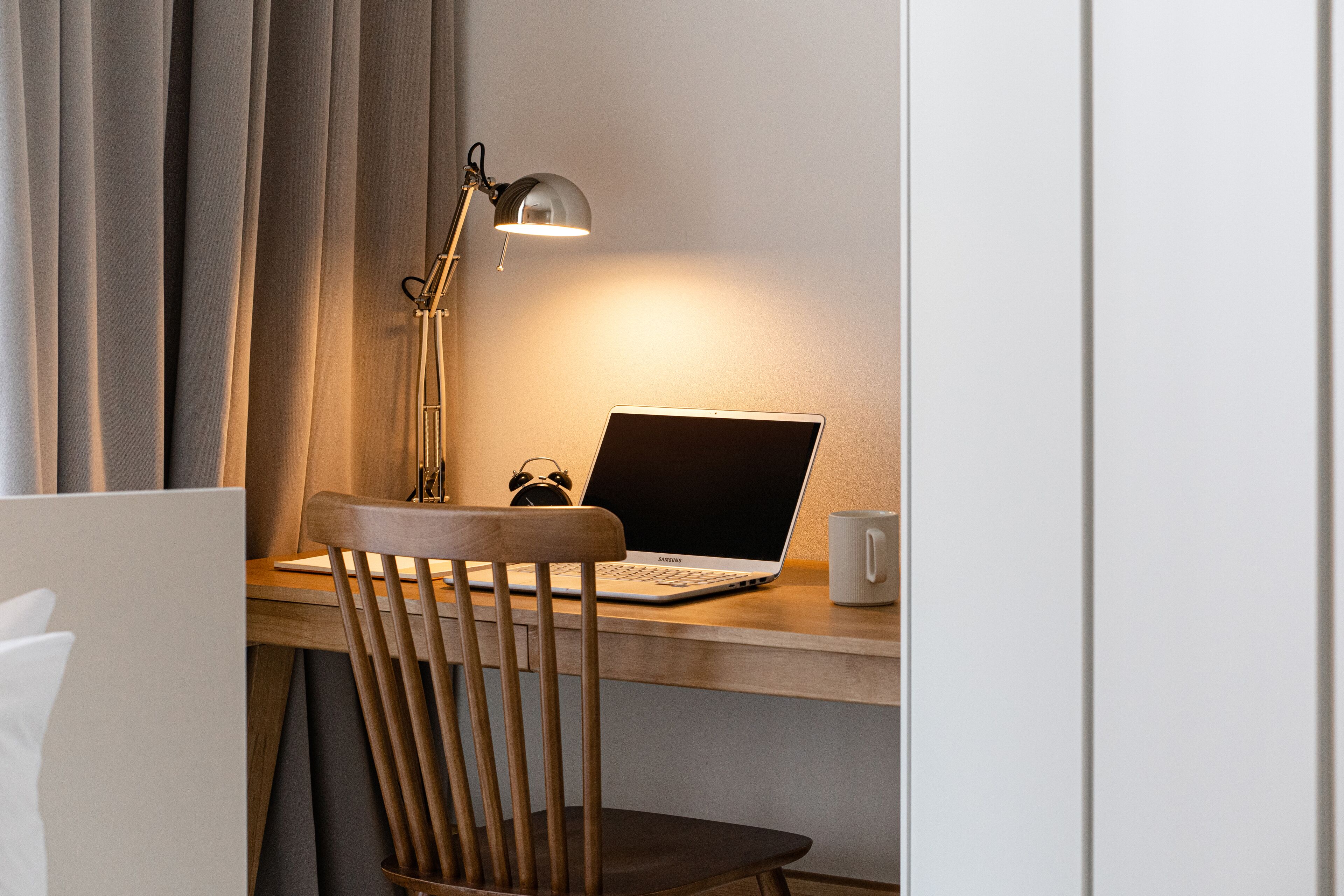 A wooden desk with a laptop, a lamp, and a white mug.