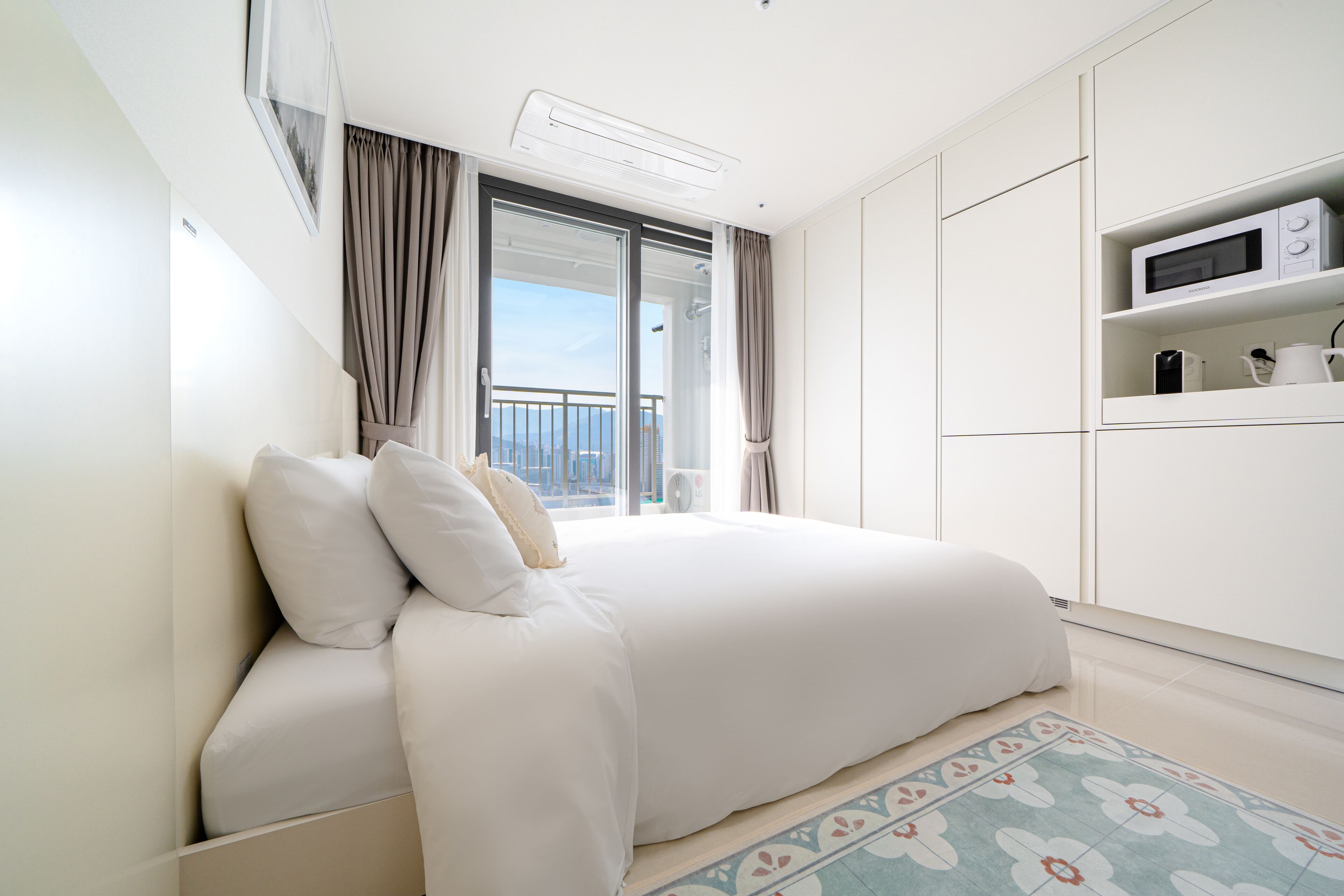 A modern bedroom with a large bed, a view of the outdoors, and a built-in microwave.