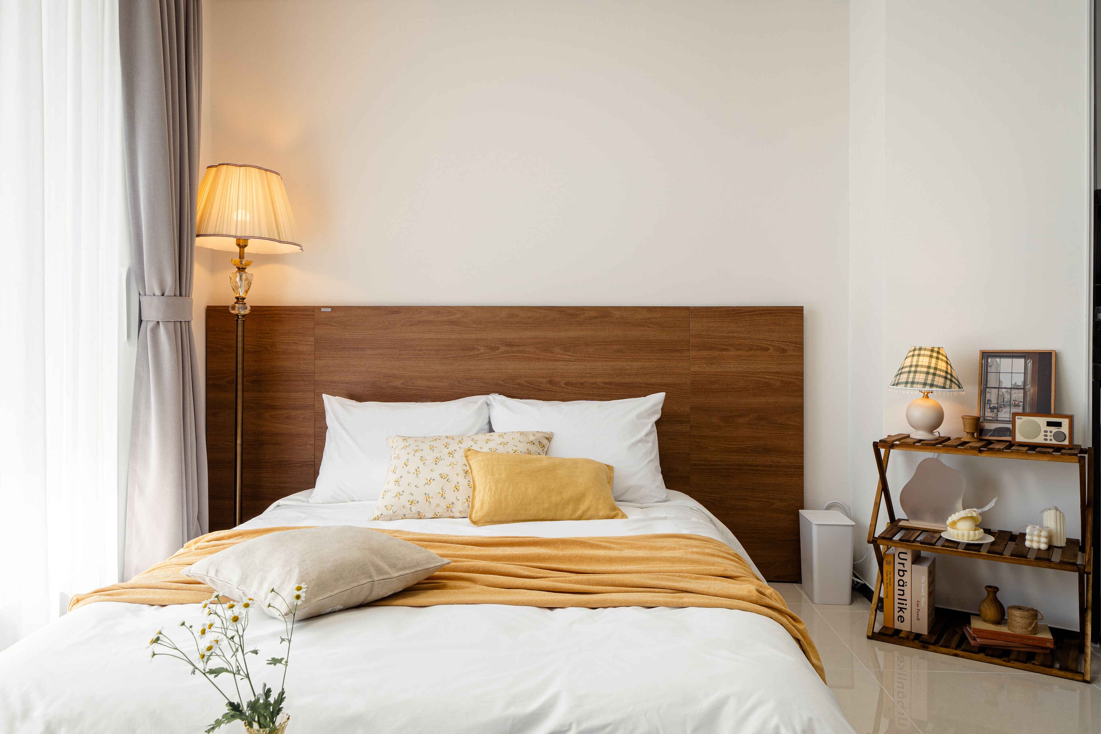 A neatly made bed with a wooden headboard, a bedside lamp, and a small wooden side table with a radio and books.