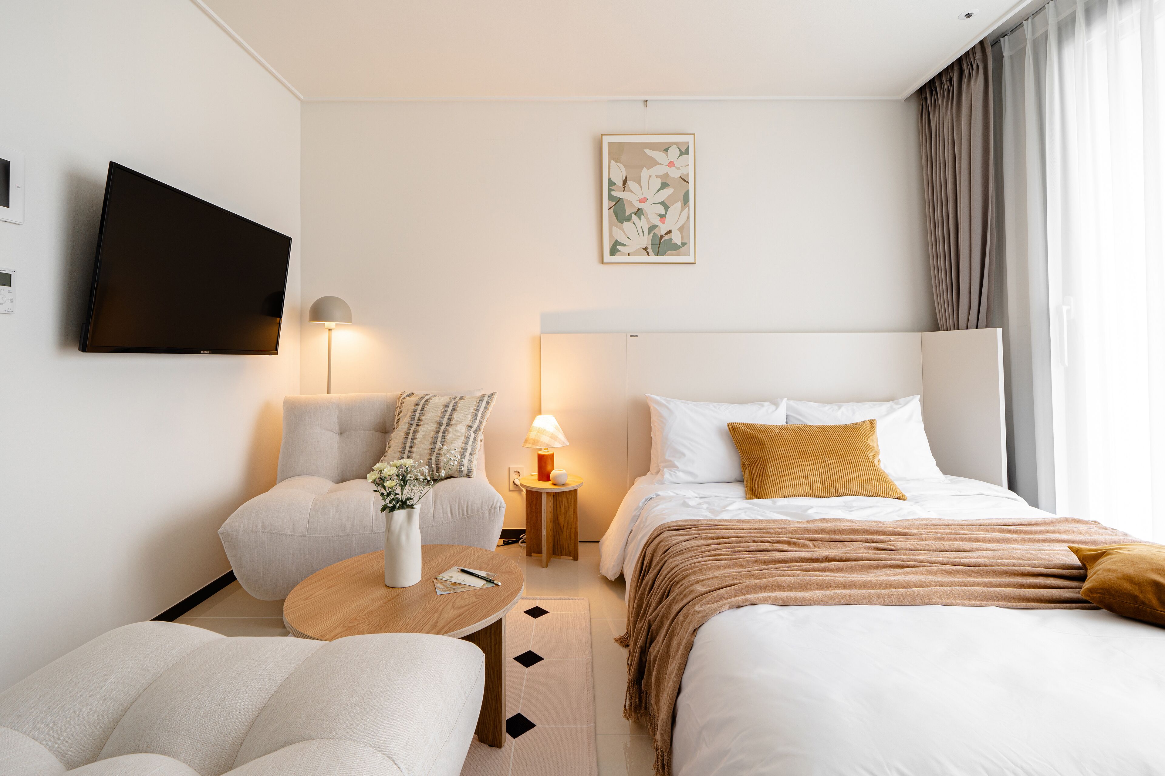 Habitación de hotel moderna con cama, dos sillones, una mesita, televisor y mesita de noche con lámpara.