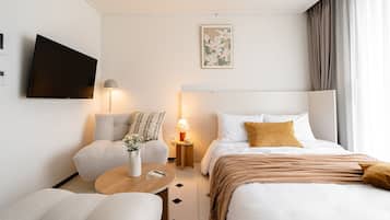 Habitación de hotel moderna con cama, dos sillones, una mesita, televisor y mesita de noche con lámpara.