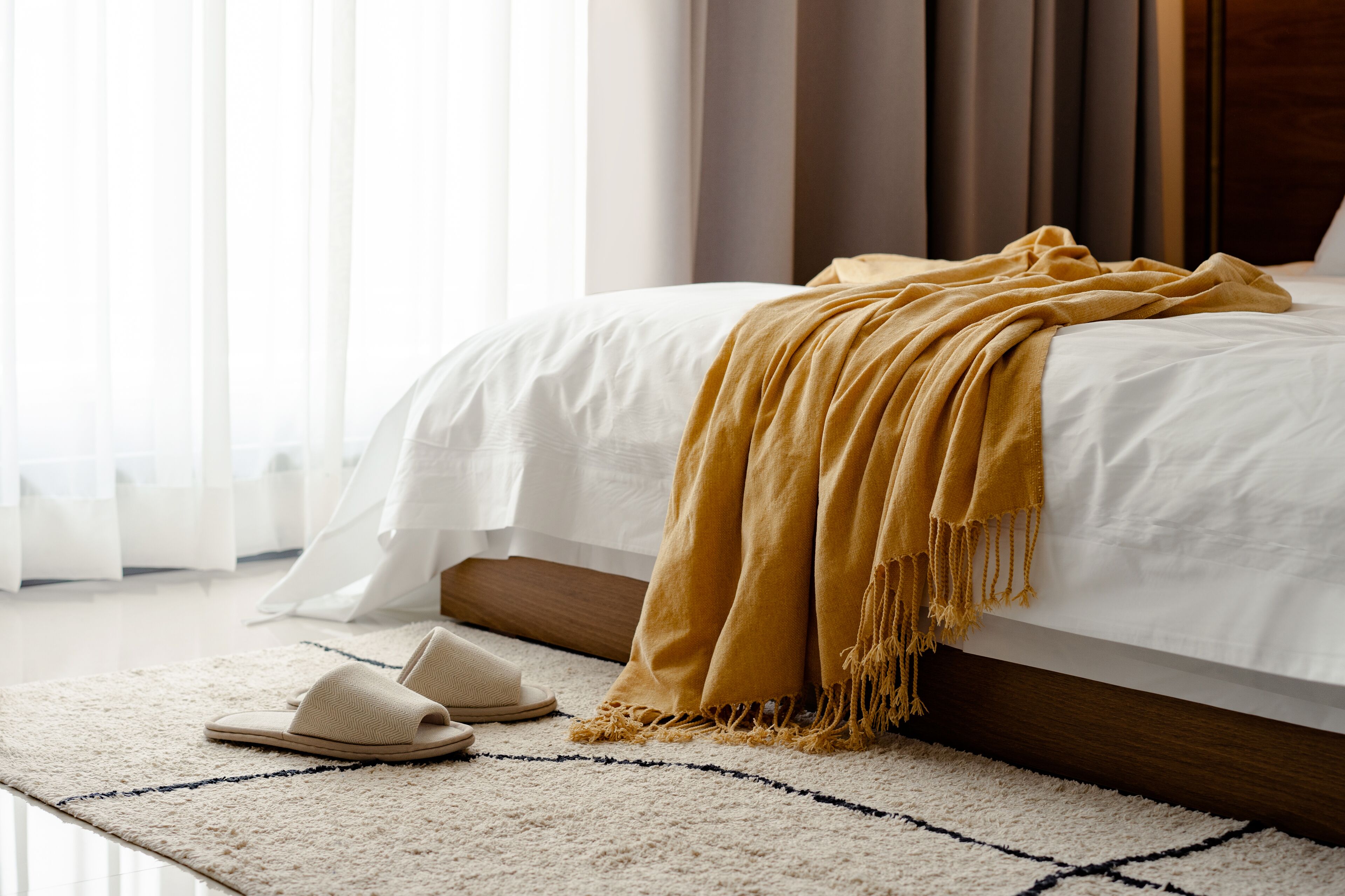 A neatly made bed with a white comforter and a mustard-colored throw blanket.
