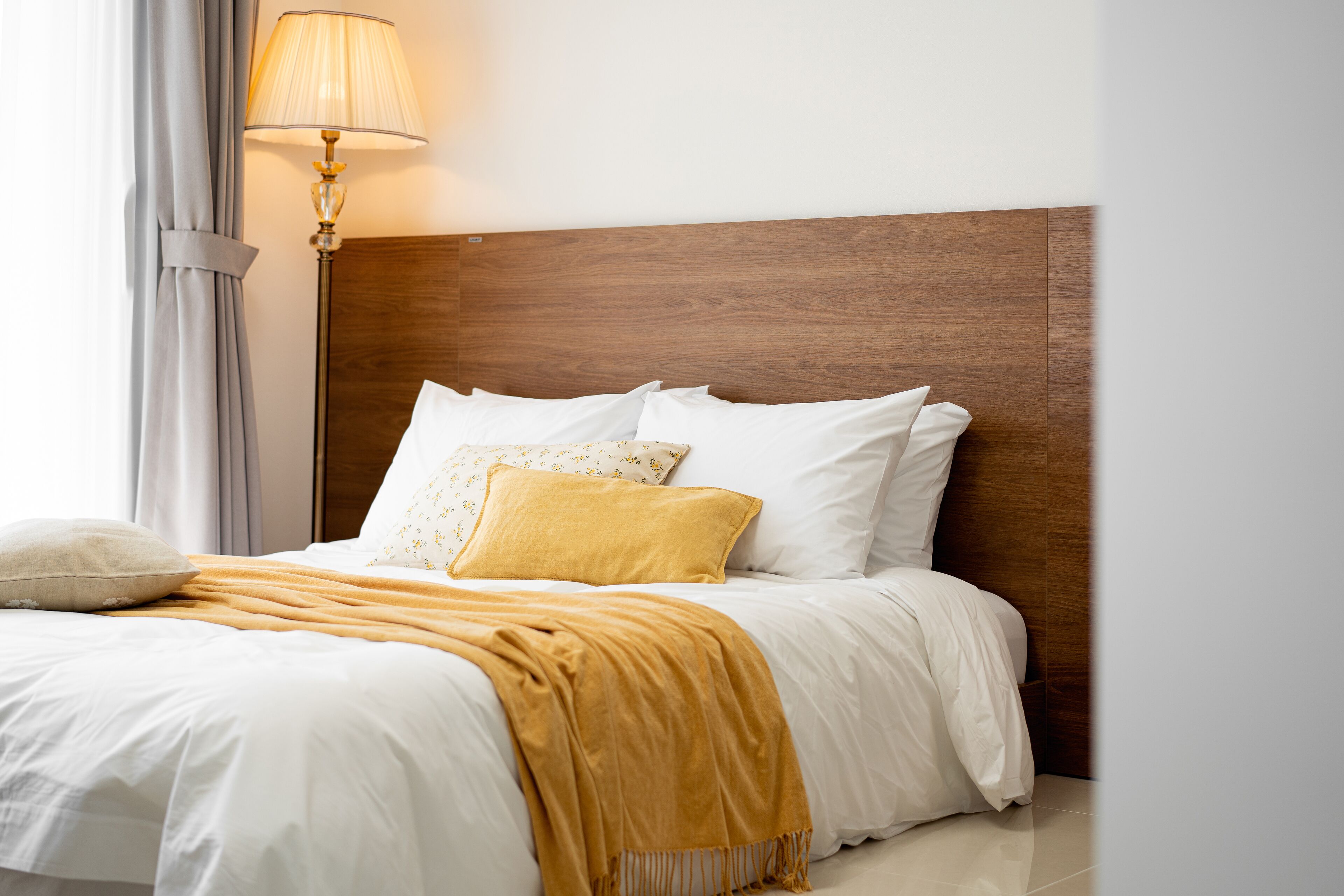 Una cama bien hecha con ropa de cama blanca y una manta color mostaza.
