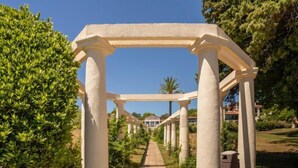 Une pergola blanche, soutenue par des colonnes, entourée de verdure et s’ouvrant sur un ciel dégagé.
