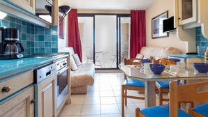 Une cuisine compacte avec des meubles bleus, une machine à café et un coin repas comprenant des chaises bleues et une table en verre.
