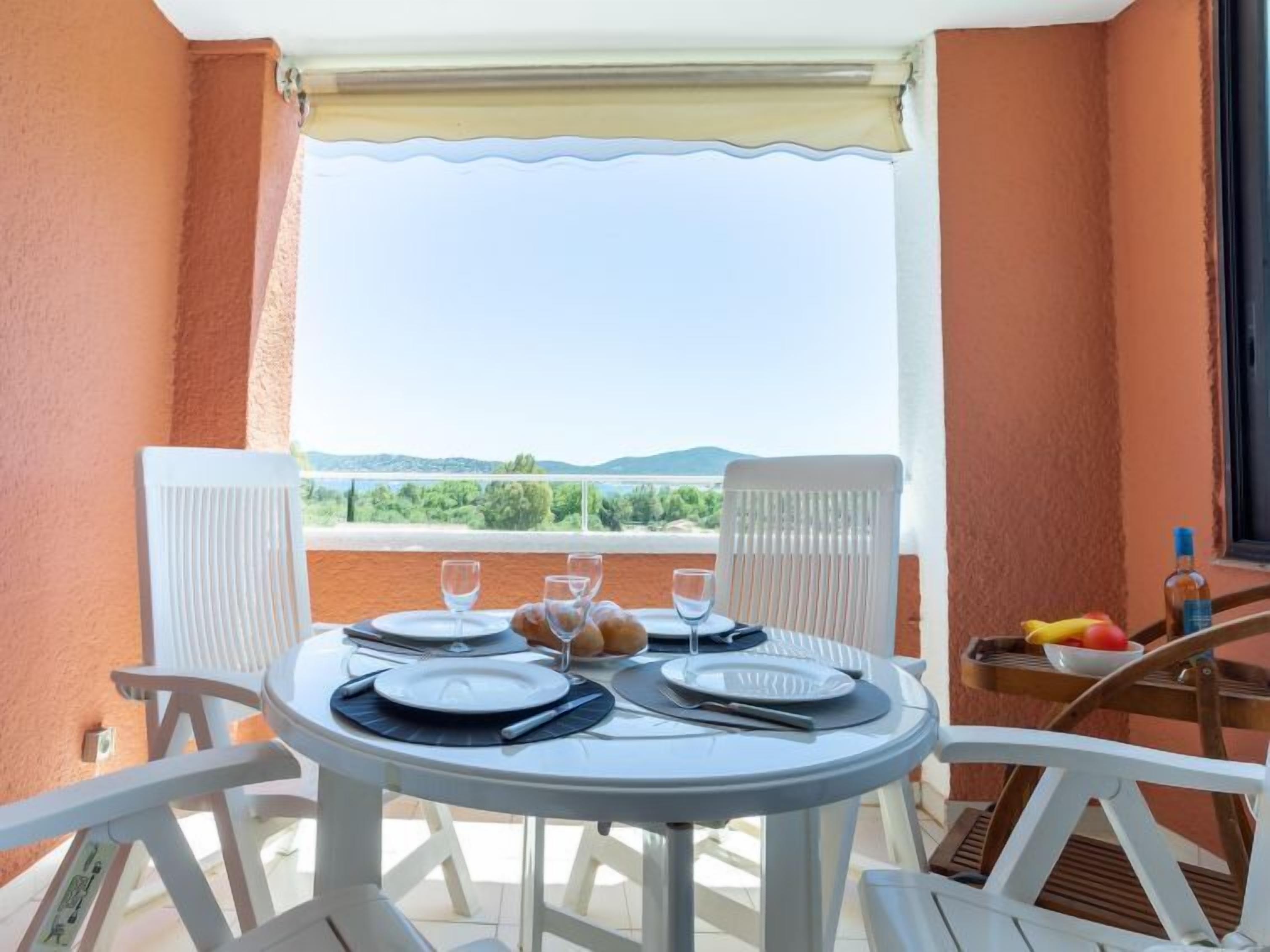 Ein Balkon mit Tisch für zwei Personen, weißen Stühlen und Blick auf Grünflächen und Hügel.