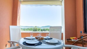 Un balcon avec une table dressée pour deux personnes, des chaises blanches et une vue sur la verdure et les collines.