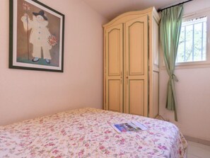 A bedroom with a floral bedspread, a framed picture on the wall, a wardrobe, and a window with curtains.