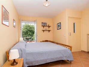 A bedroom with a bed, a bedside table with a lamp, a window, and a door leading to a balcony.