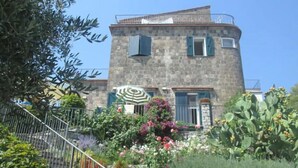 Un bâtiment en pierre doté d’un balcon, entouré d’une végétation luxuriante et de plantes en fleurs.