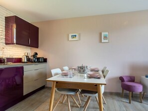 Une cuisine moderne avec une table à manger dressée pour quatre personnes, agrémentée d’une nappe blanche, d’assiettes roses et de verres transparents.