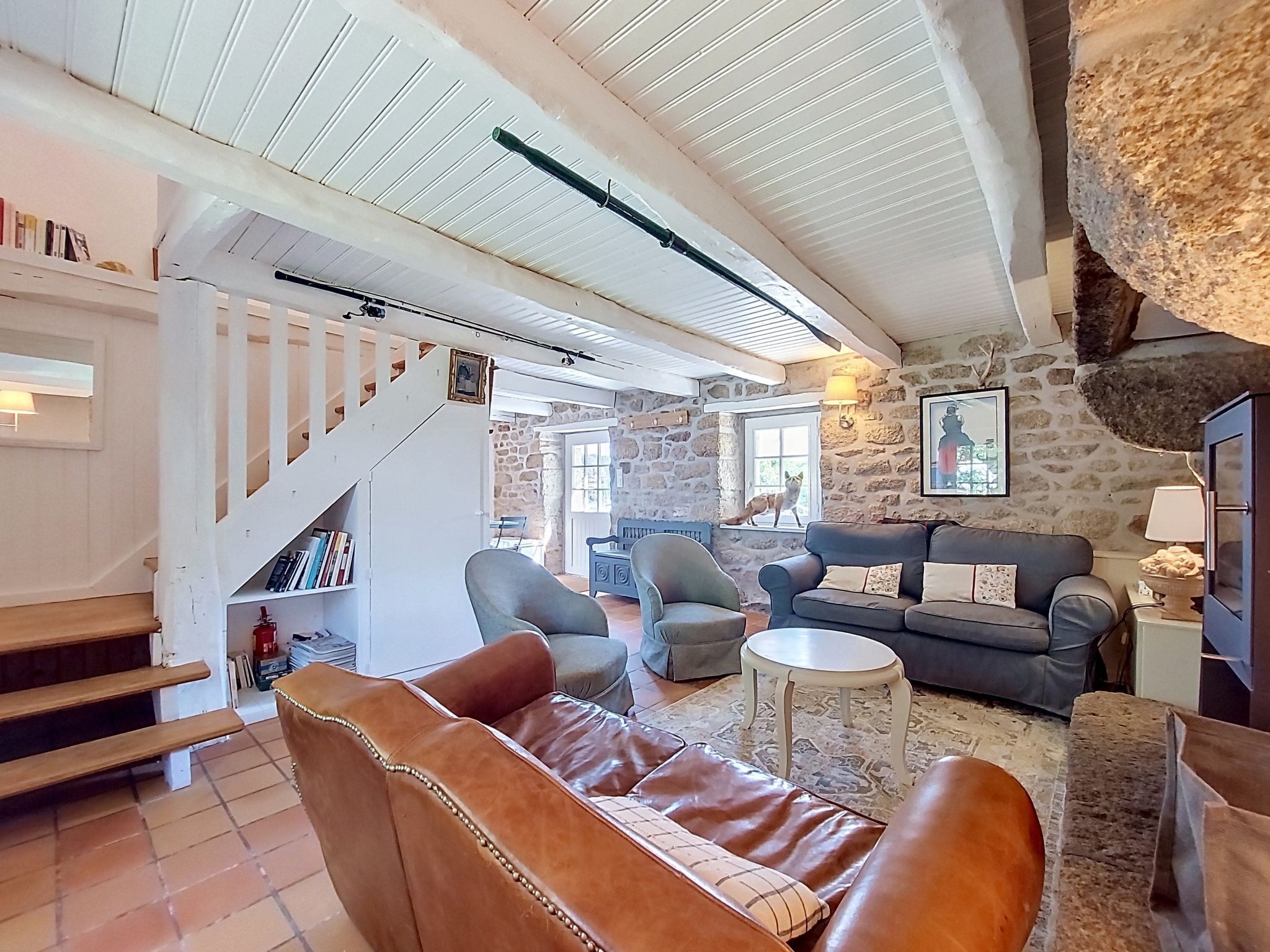 A spacious living area with a stone wall, a fireplace, leather sofas, and a staircase.
