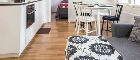 Een knus woongedeelte met een kitchenette, een eethoek met een ronde tafel en stoelen, en een bank met een decoratief plaid.