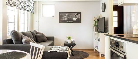 A modern living room with a sofa, a dining table, a kitchen area with an oven, and a framed picture of a bridge.