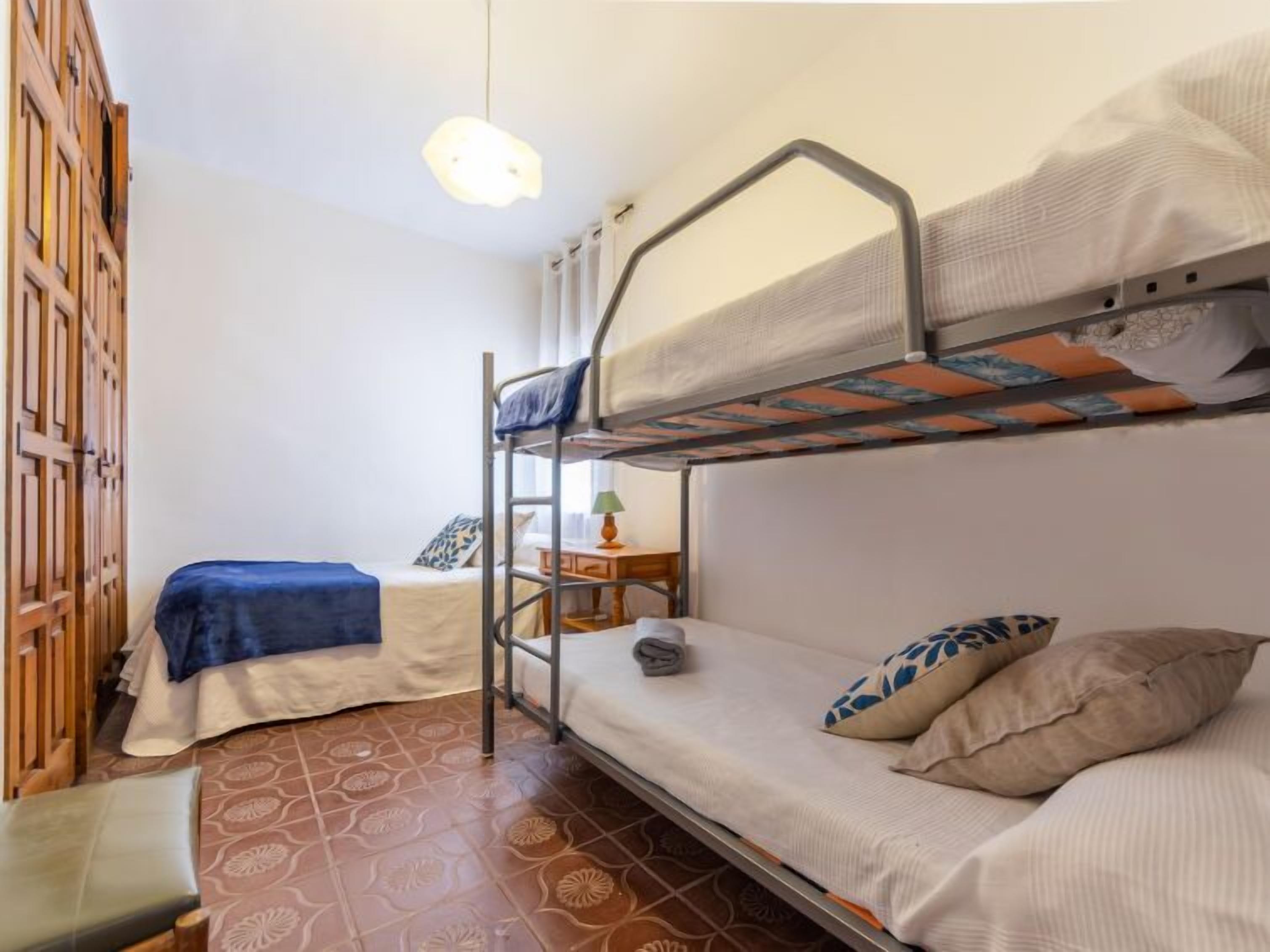 A dormitory room with bunk beds, a small table with a lamp, and a patterned floor.