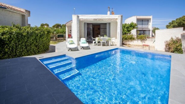 A modern poolside area with a clear blue pool, a covered seating area, and a white building with a tiled roof. - Vacation home Moru by Interhome (Deltebre)