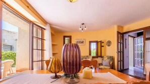 A dining area with a wooden table, two chairs, and a vase. There is a window with curtains and a door leading to another room. - Vacation home Moru by Interhome (Deltebre)