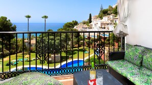 Ein Balkon mit Blick auf einen Swimmingpool und das Meer, ausgestattet mit einer Couch und einem Tisch.