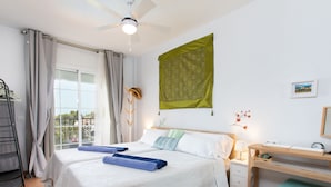 Ein Hotelzimmer mit zwei Betten, einem Schreibtisch, einem Stuhl, einem Kleiderschrank und einem Balkon mit Blick.