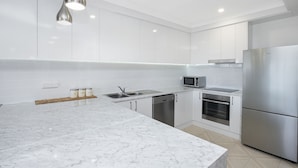 A modern kitchen with white cabinets, stainless steel appliances, and a marble countertop.