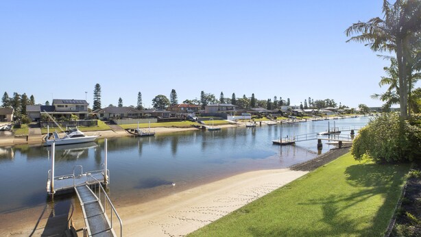 A marina with boats docked, a sandy beach, and houses in the background.